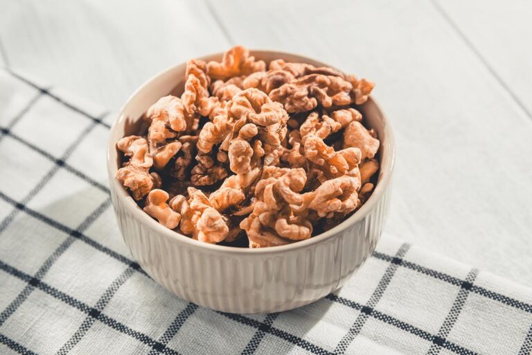 A white porcelain bowl filled with specialty crop walnuts sits on a table