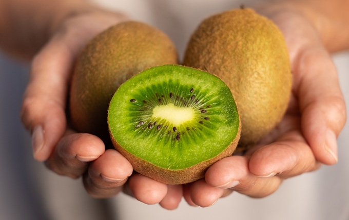 Hands holding sliced green kiwifruit
